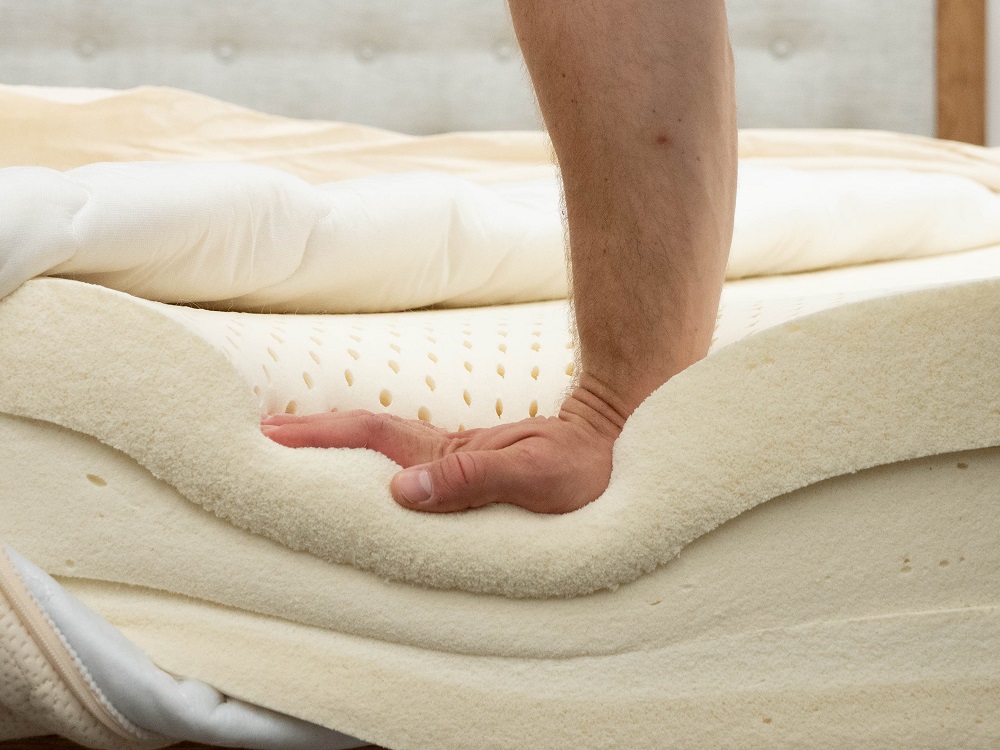 A hand pressing down into the layers of a mattress.