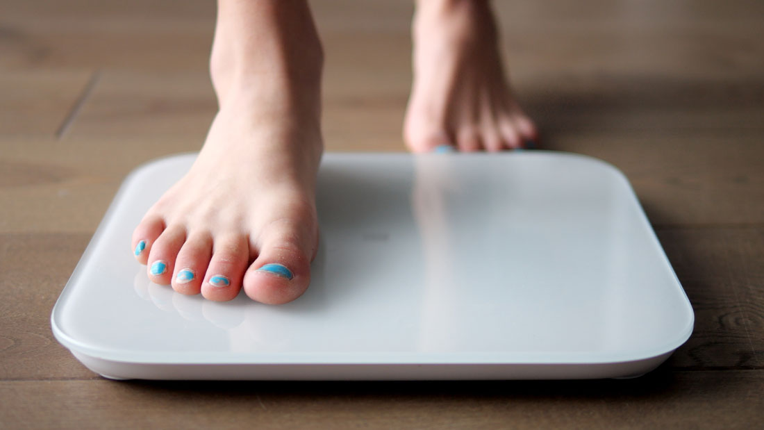 elderly woman standing barefoot on a bathroom scale and measuring