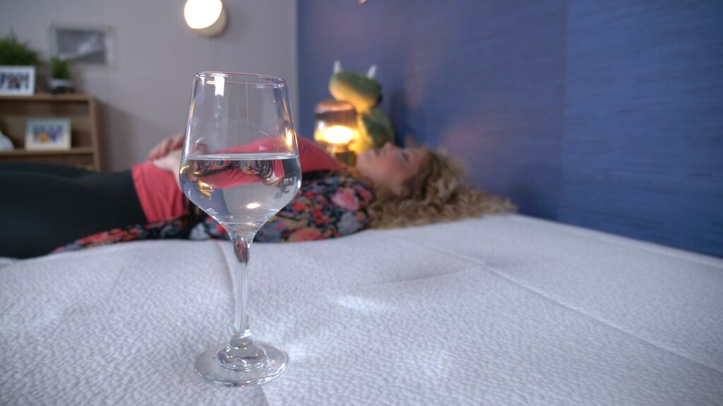 A woman lying on a mattress next to a wine glass full of water.