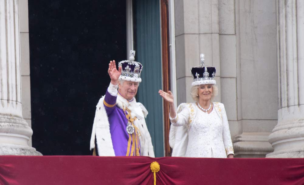 king charles and queen camilla waving from a balcony