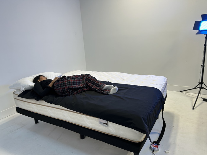 A lightweight woman lying on her side on top of a pressure mat draped over the Saatva mattress.