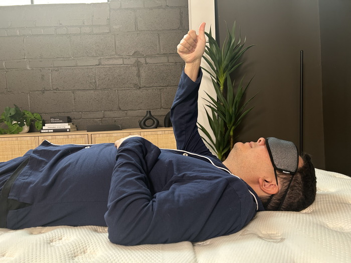 A man lying on the Saatva. He's wearing a blindfold and giving a thumbs up to indicate when he can feel his partner moving around.