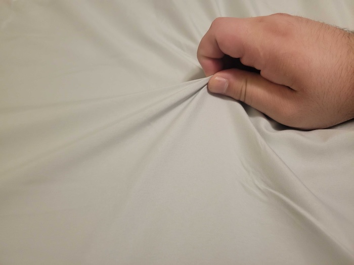 A hand pinches a sheet from the Mellanni Iconic Collection.