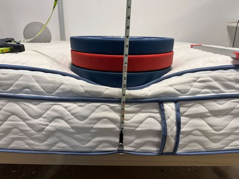 Our tester measures weight plate deflection on the edge of a DLX Hybrid mattress