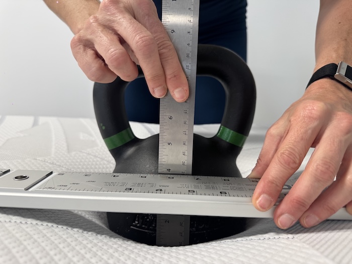 A kettlebell resting on the BodiPedic 12" mattress. A woman measures the sinkage.
