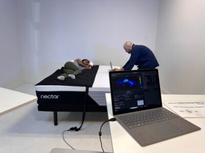 A woman lies on a pressure mat on the Nectar Premier mattress as a man types on his laptop on the other side of the bed