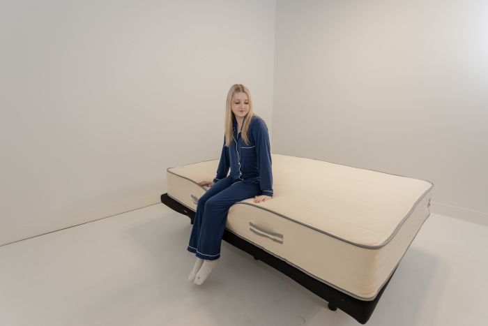 A woman sitting on the edge of the Nolah Natural mattress to test its edge support.