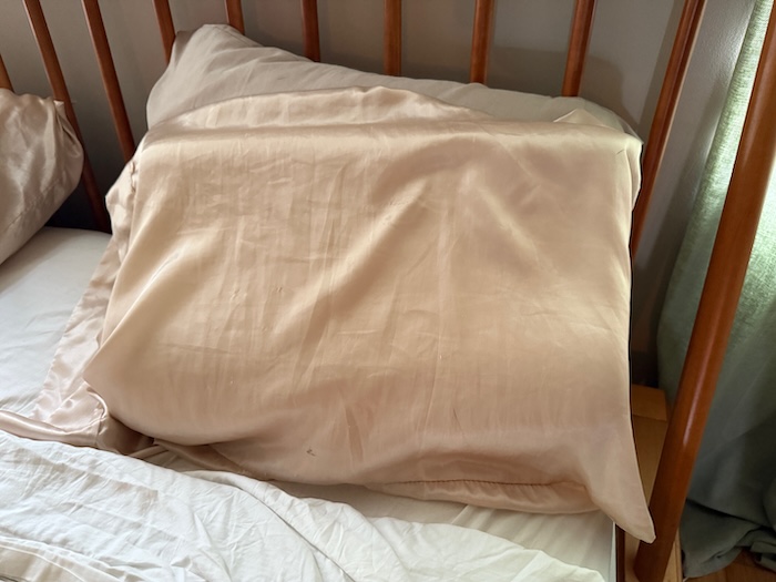 A Tempur-Neck Pillow sitting on a bed, in its pillowcase.