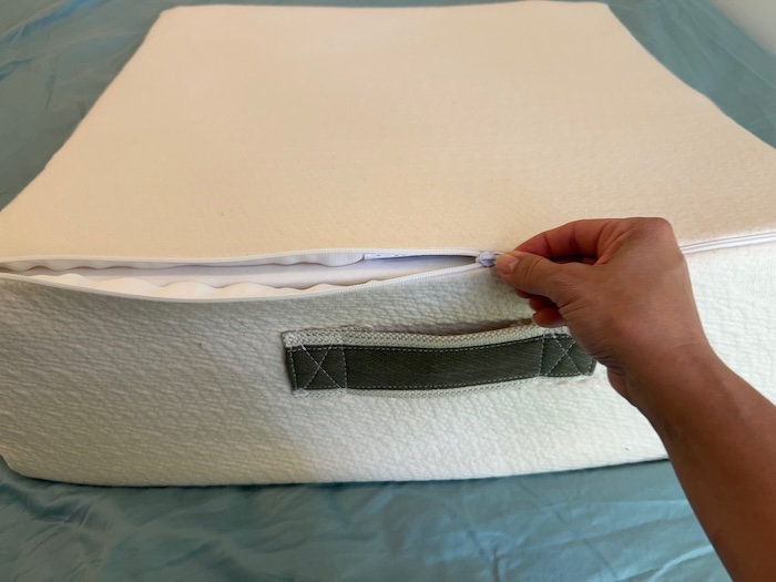 A hand unzipping the cover of the Avocado Wedge Pillow.