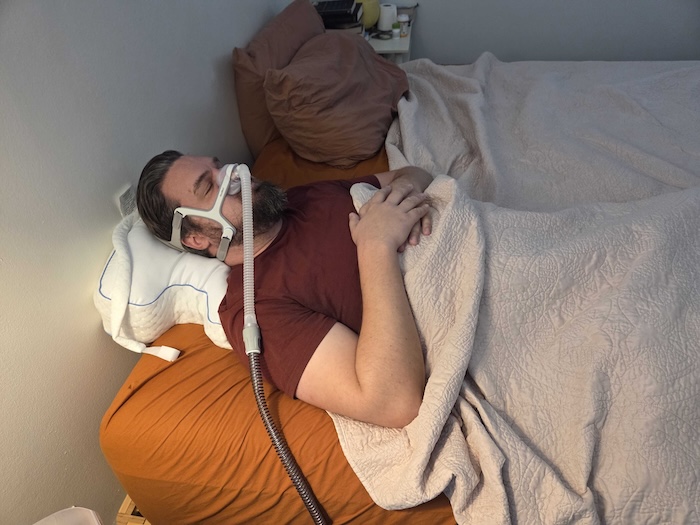 A man sleeping on his back on the Contour pillow. He's wearing a sleep apnea mask as he dozes.