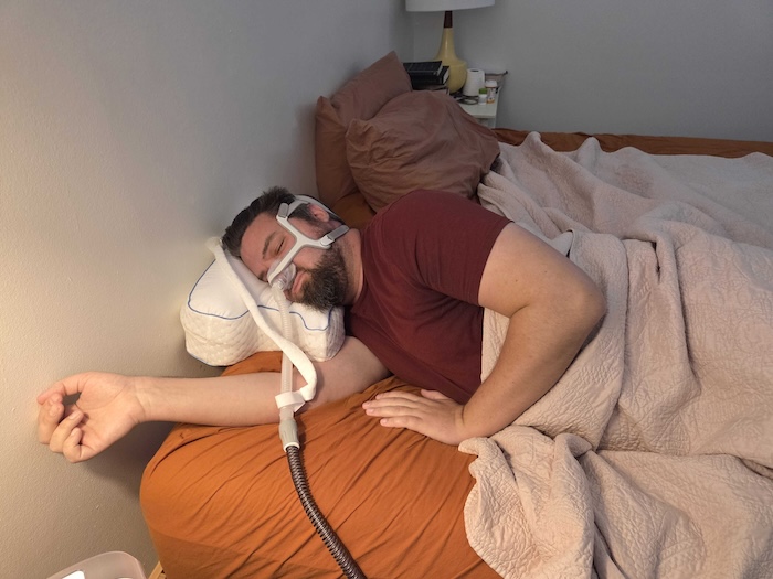 A man sleeping on his side on the Contour pillow. He's wearing a sleep apnea mask as he dozes.