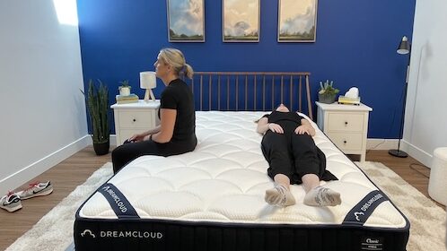 A woman sits on the edge of the DreamCloud mattress while another woman lies next to her.