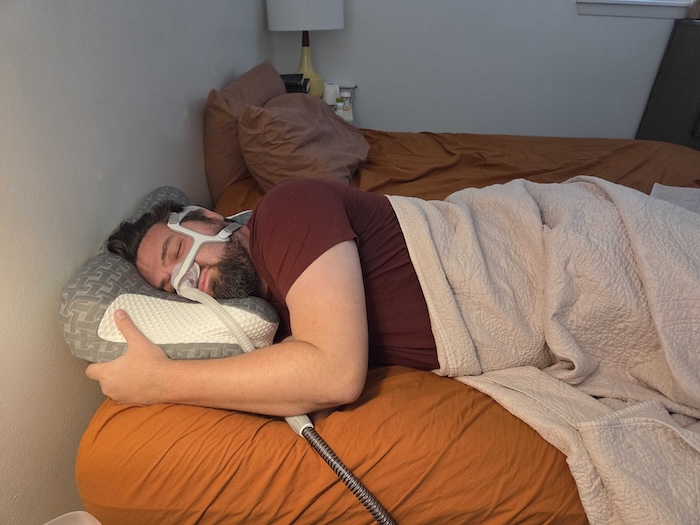 A man sleeping on his side on the Elviros pillow. He's wearing a sleep apnea mask as he dozes.
