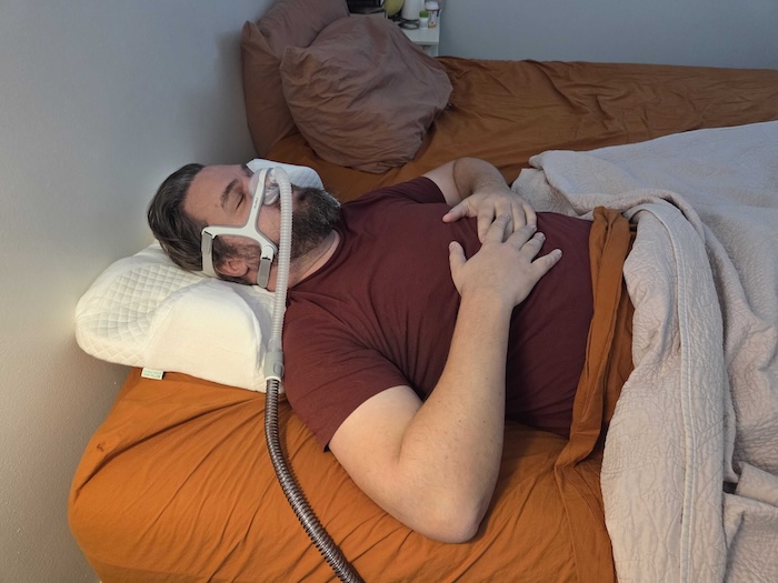 A man sleeping on his back on the Endurimed pillow. He's wearing a sleep apnea mask as he dozes.