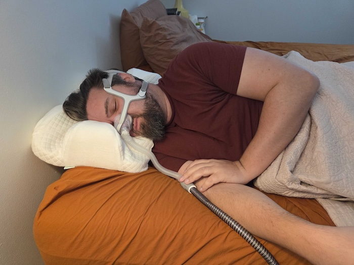 A man sleeping on his side on the Endurimed pillow. He's wearing a sleep apnea mask as he dozes.