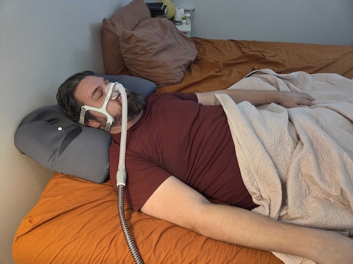 A man sleeping on his back on the Ikstar pillow. He's wearing a sleep apnea mask as he dozes.