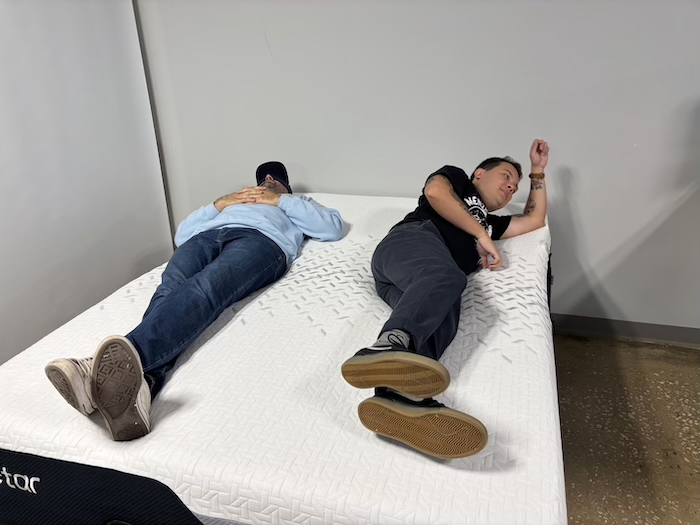 Two men lying on a Nectar Premier Memory Foam mattress. One of them is rolling over to test the bed's motion isolation.