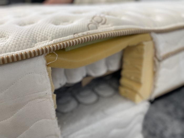 A view of the Saatva mattress from the side. A section has been cut out, showing the construction of foam and innerspring coils underneath.