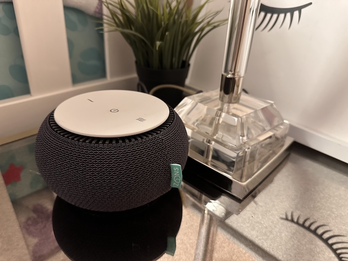 A closeup of a Snooz White Noise Machine sitting next to a lamp.