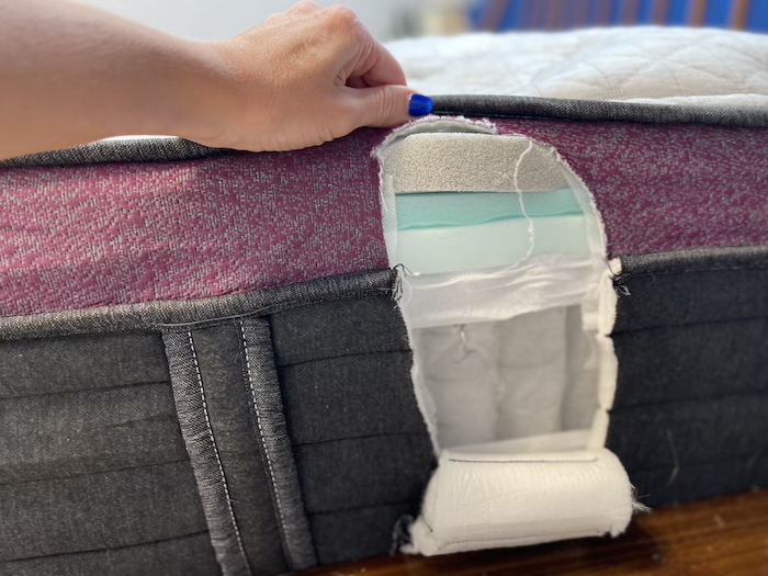 A closeup of the side of the Helix Dusk Luxe mattress. A section has been cut out, showing the layers of foam and coils underneath.